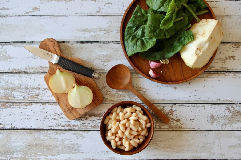 Rustic Tuscan white bean soup with wilted spinach, served in a speckled ceramic bowl with toasted bread on a wooden board