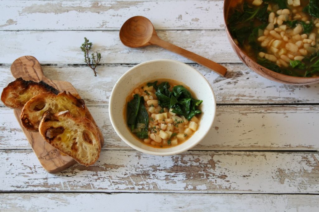 Close-up of creamy Tuscan white bean soup with fresh spinach, thyme, and cubed vegetables, served in a deep white bowl
