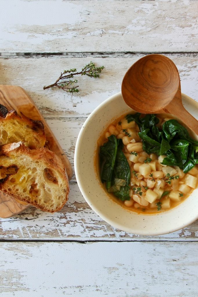 Wide shot of a hearty Tuscan white bean soup with fresh spinach and toasted bread, served on a rustic wooden table